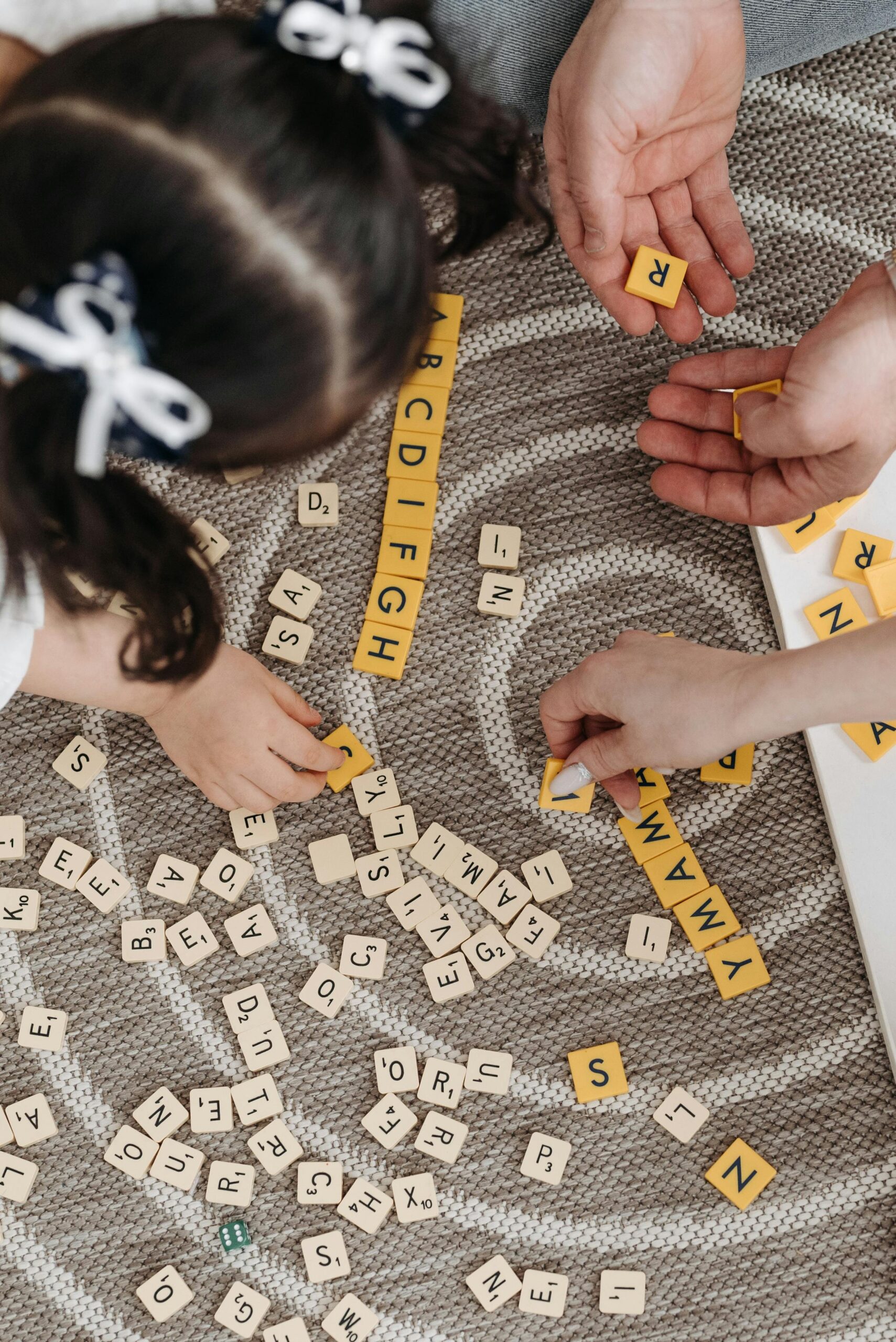 Family playing a word game with tiles on a patterned carpet, showcasing togetherness and learning.